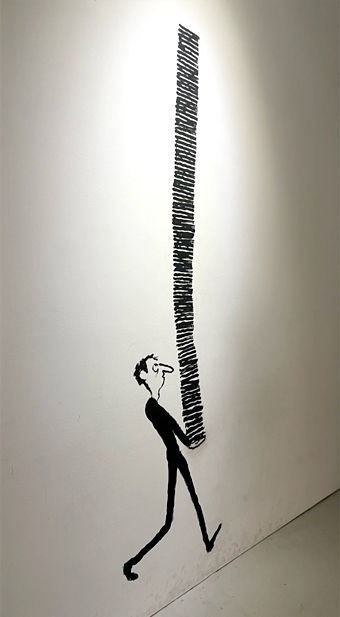 단순한 검정색 선으로 그려진 벽화. 한 남자가 키의 두 배가 넘는 높이로 쌓은 무언가를 들고 걷고 있다.