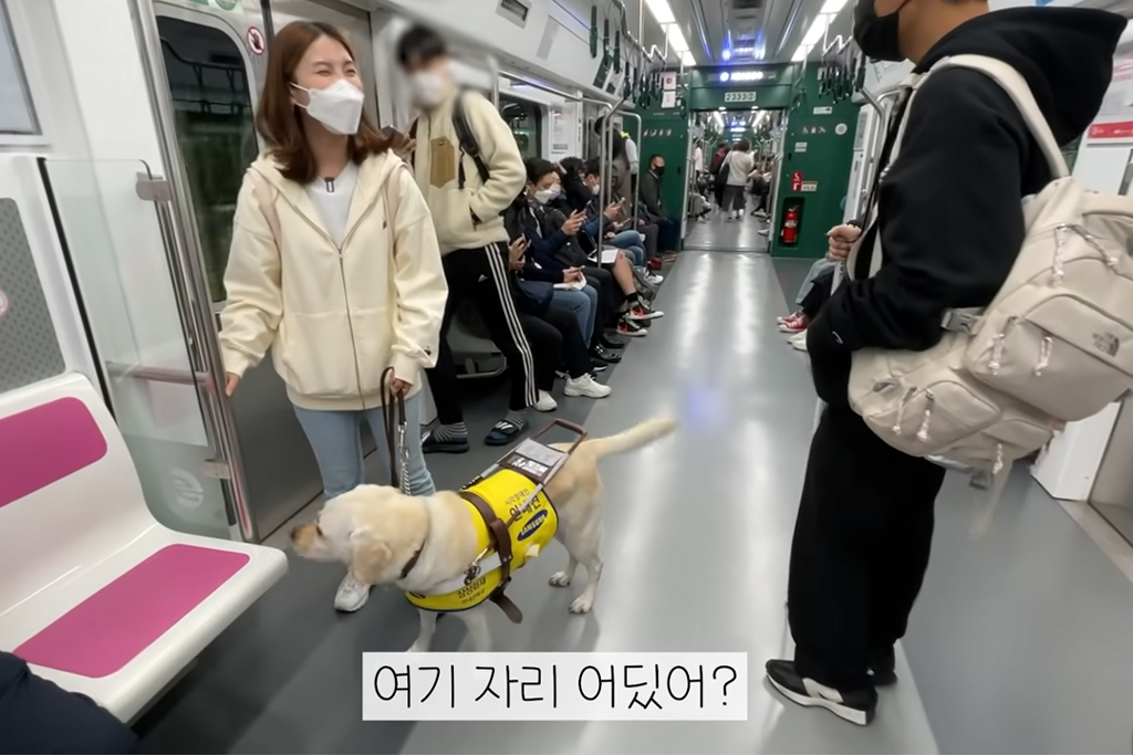 우령의 유디오 유튜브 영상 캡처. 시각장애인 우령의 유디오가 안내견과 같이 지하철 안에서 좌석을 찾고 있다.