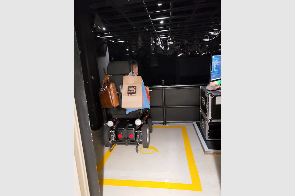 어두운 극장 안 윗층. 펜스 안쪽 바닥에 노락색으로 휠체어석이 표시된 장애인석이다.