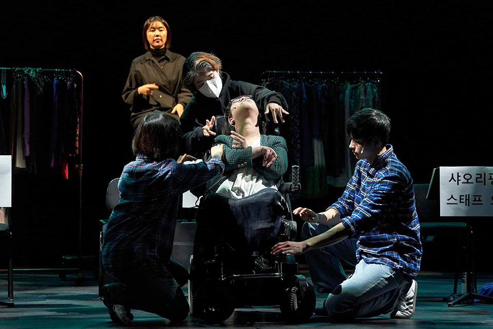 ‘청즈’가 휠체어에 앉아 몸을 뒤로 젖히고 있고, 세 명의 배우가 ‘청즈’에게 양팔을 뻗으며 둘러싸고 있다. 뒤에는 수어통역사가 있다.