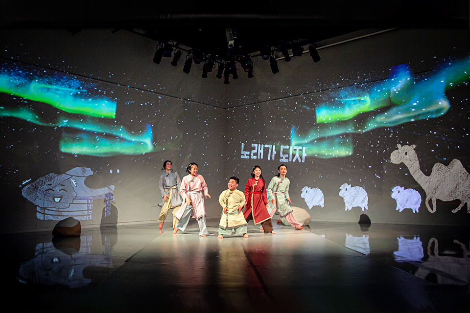 다섯 명의 배우가 무대에 나란히 서 있다. 한가운데가 김유남 배우다. 벽에는 오로라와 양들, 낙타 그림이 영사되고 있다.