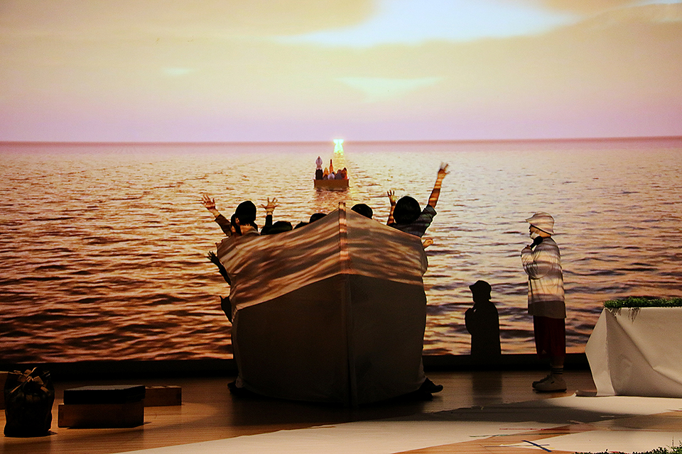 무대에는 배 모형의 소품에 배우들이 타고 있고, 벽면에는 수평선의 바다가 영사되고 있다.