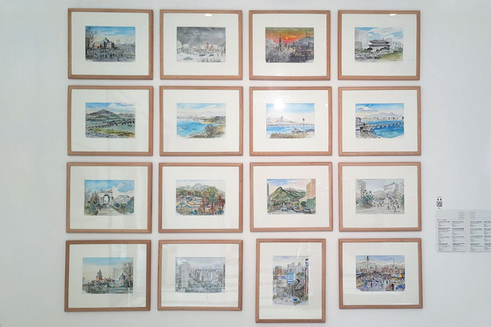 전시장 벽에 도시 풍경을 담은 작은 수채화 그림이 담긴 나무액자 16점이 네 줄로 배열되어 있다.