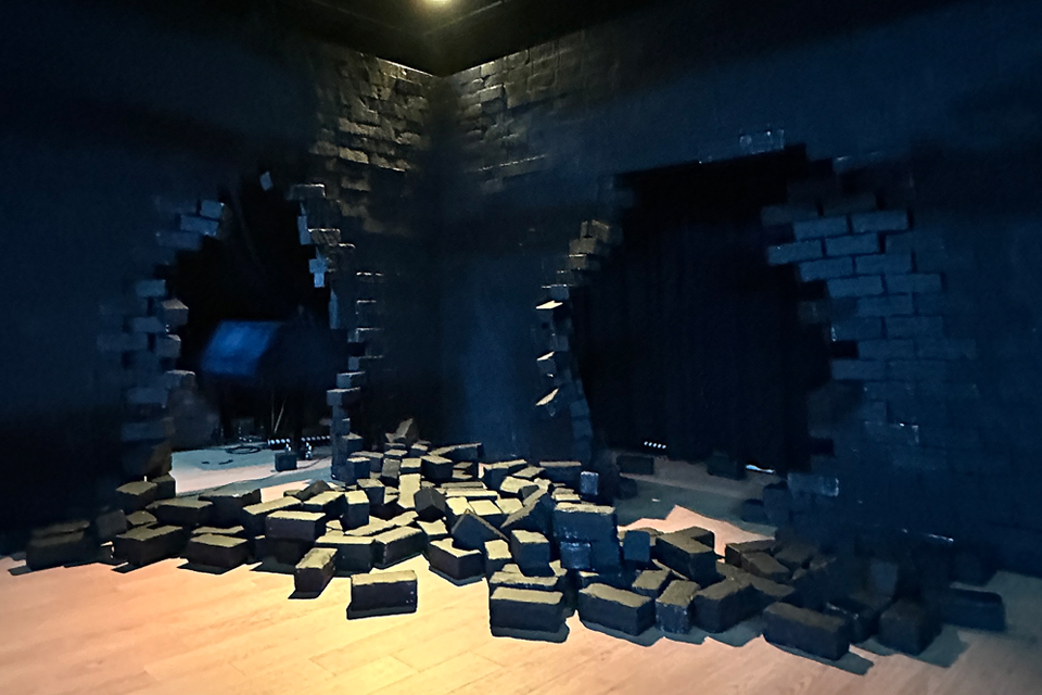 검은 벽이 무너져 벽돌이 바닥에 흩어진 무대 세트 장면