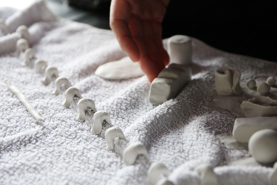 흰색 타월 위에 지점토로 만든 크기와 형태가 다른 흰색의 작은 조각들이 줄지어 또는 흩어져 있고, 한 손으로 조각을 만지고 있다.