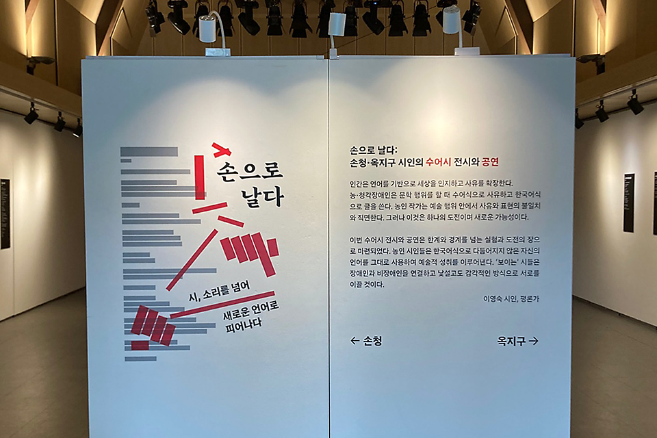 전시장 입구 전경. 중앙에 전시 소개문이 적힌 가벽이 세워져 있고, 전시장 벽에 시가 적힌 보드가 붙어 있다.