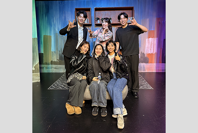 무대 세트 앞에서 배우와 관객이 함께 기념사진을 찍고 있다. 뒷줄에 선 세 배우는 수어로 ‘사랑해(ILY)’ 손동작을 하고 있다. 그 앞에 놓인 소파에 앉은 세 명의 관객도 카메라를 향해 미소 짓고 있다.