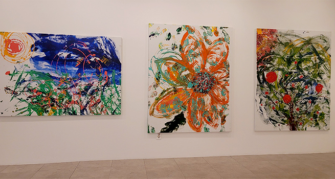 대형 회화 세 점이 벽에 나란히 걸려 있다. 왼쪽은 노란 해와 푸른 하늘, 초록빛 붓질이 뒤섞인 풍경 같고, 가운데는 굵은 붓 터치로 그린 커다란 주황색 꽃, 오른쪽은 붉은 열매가 달린 나무 형태가 추상적으로 표현돼 있다.