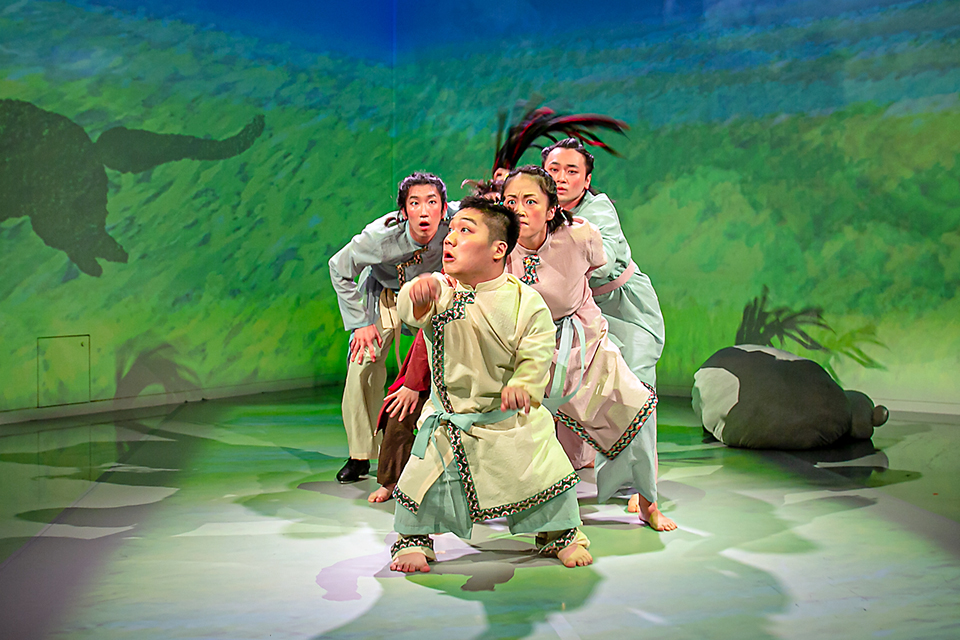 김유남 배우를 선두로 네 명의 배우가 줄지어 서 있다. 배우들은 초록색 풀밭과 동물 그림자가 프로젝션된 배경에서 연기하고 있다. 