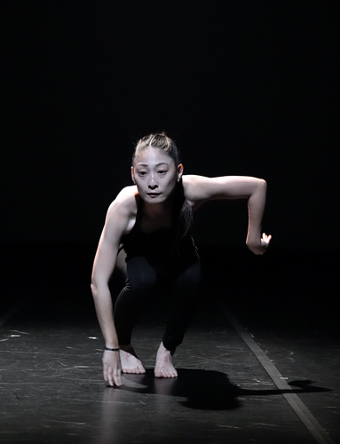 어두운 무대 위에서 타이트한 검정색 의상을 입은 김소영이 낮은 자세로 몸을 웅크린 채 두 팔을 비대칭적으로 뻗고 있다.