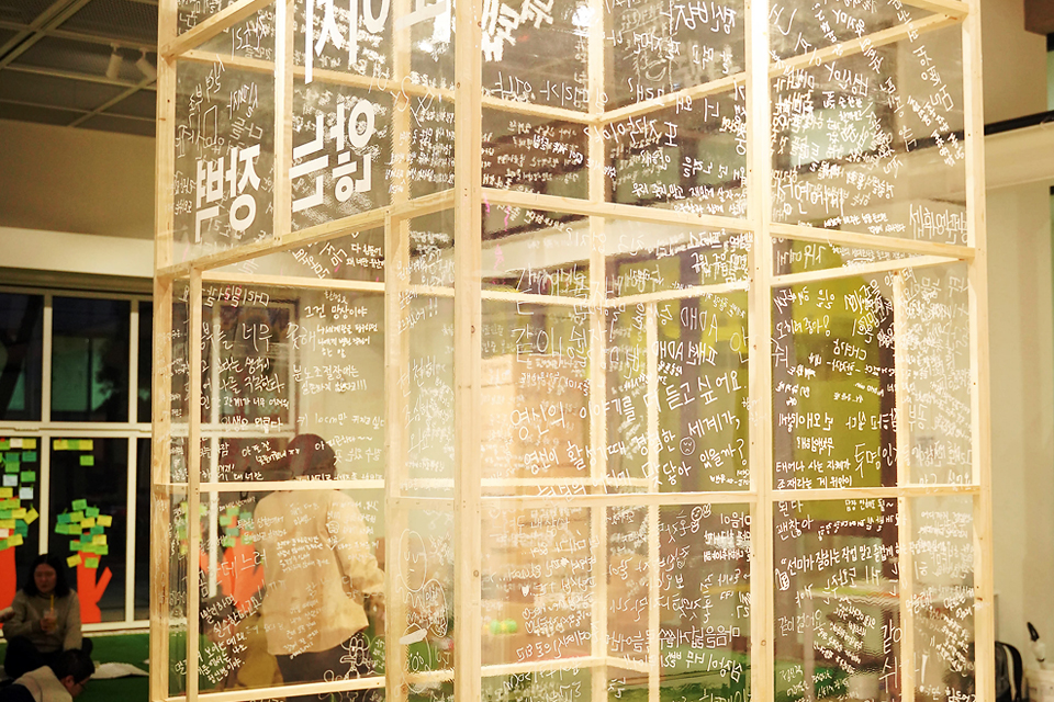 투명 아크릴판을 나무 프레임으로 세운 설치미술 작품이 전시장 중앙에 서 있다. 사방의 투명한 벽면에는 흰색 글씨로 다양한 감정과 경험이 빼곡히 적혀 있고, 바깥쪽에는 돌봄과 연대의 메시지가 적혀 있다.