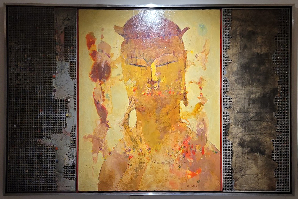 대체텍스트 중앙에는 노란색 바탕 위에 붉은색과 주황색이 겹겹이 스며든 부처의 얼굴 형상이 표현되어 있다. 좌우에는 거칠고 어두운 색감의 패널이 함께 배치되어, 중심 이미지와 대비를 이루며 작품의 긴장감을 더한다.