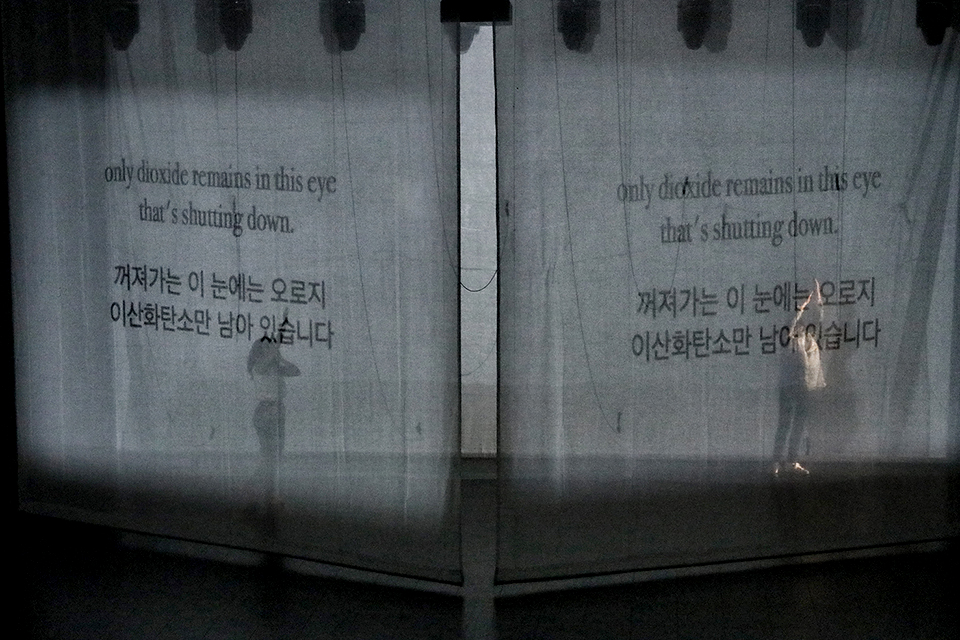 얇은 막 뒤편에 양쪽으로 에바나와 힐다가 서 있는 모습이 흐릿하게 비친다. 얇은 막에는 ‘꺼져가는 이 눈에는 오로지 이산화탄소만 남아있습니다’라는 글씨가 한국어와 영어로 투사되고 있다.