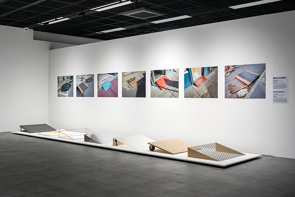 전시장 바닥에 여러 형태와 재질의 경사로 조형물 일곱 개가 줄지어 설치되어 있다. 뒤편 벽에는 〈캘거리의 경사로〉 사진 작품 일곱 장이 일렬로 전시되어 있다.