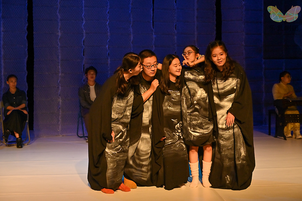 무대 중앙에 검은 옷을 입은 출연자들이 서로 몸을 밀착해 서 있다. 각자의 검은 의상 위에는 태아를 상징하는 그림이 그려져 있다.