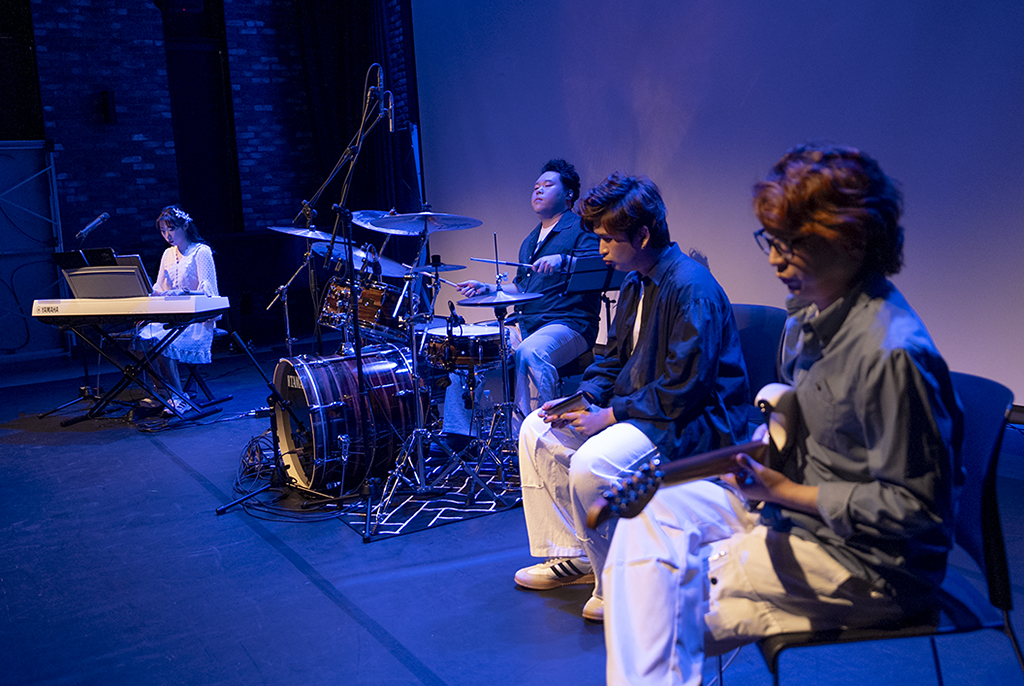 푸른색 조명 아래 우박이지 밴드가 연주하고 있다. 무대 왼쪽에 서지은이 키보드를 연주하고, 옆으로 나란히 드럼 스틱을 쥔 박호진이 드럼을, 이인혁이 하모니카를, 우병욱이 일렉기타를 연주하고 있다.