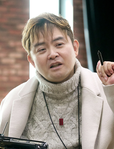 붉은 벽돌벽에 세로로 길게 난 창을 배경으로 다섯 명이 미소 지으며 카메라를 바라보고 있다. 앞의 두 사람은 휠체어에 앉아 있고, 뒤의 세 사람은 서 있다.