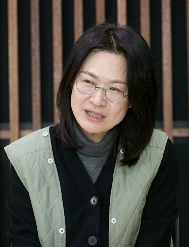 붉은 벽돌벽에 세로로 길게 난 창을 배경으로 다섯 명이 미소 지으며 카메라를 바라보고 있다. 앞의 두 사람은 휠체어에 앉아 있고, 뒤의 세 사람은 서 있다.