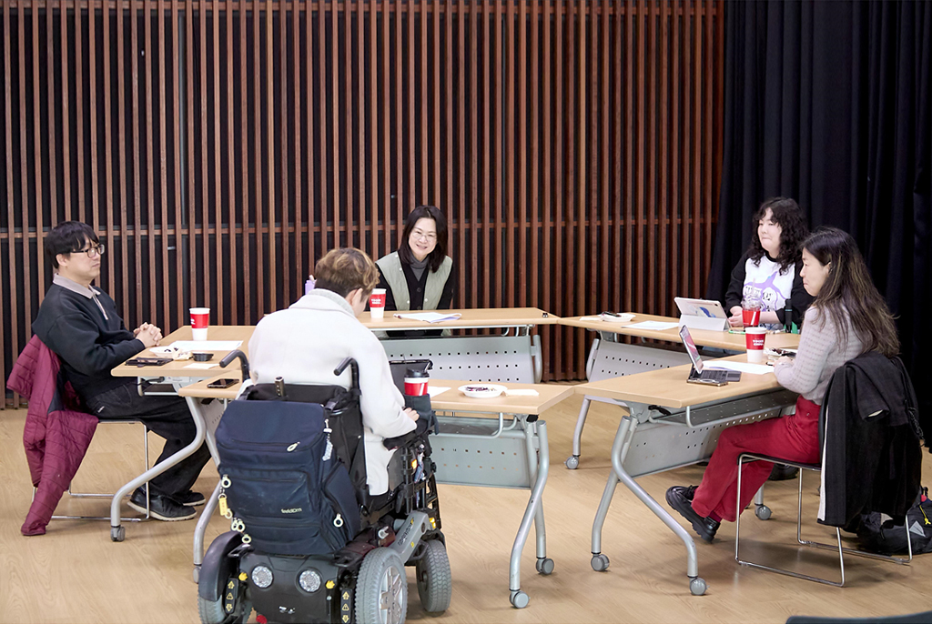 다섯 명의 참여자가 오각형으로 놓은 테이블 앞에 앉자 이야기 나누고 있다.