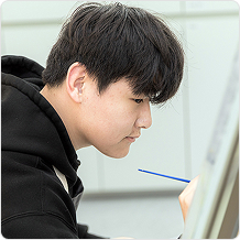 검정색 후드티를 입은 남성이 이젤 앞에서 그림을 그리는 옆모습