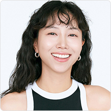 긴 곱슬머리에 검정색 민소매티를 입은 여성이 활짝 웃고 있다.